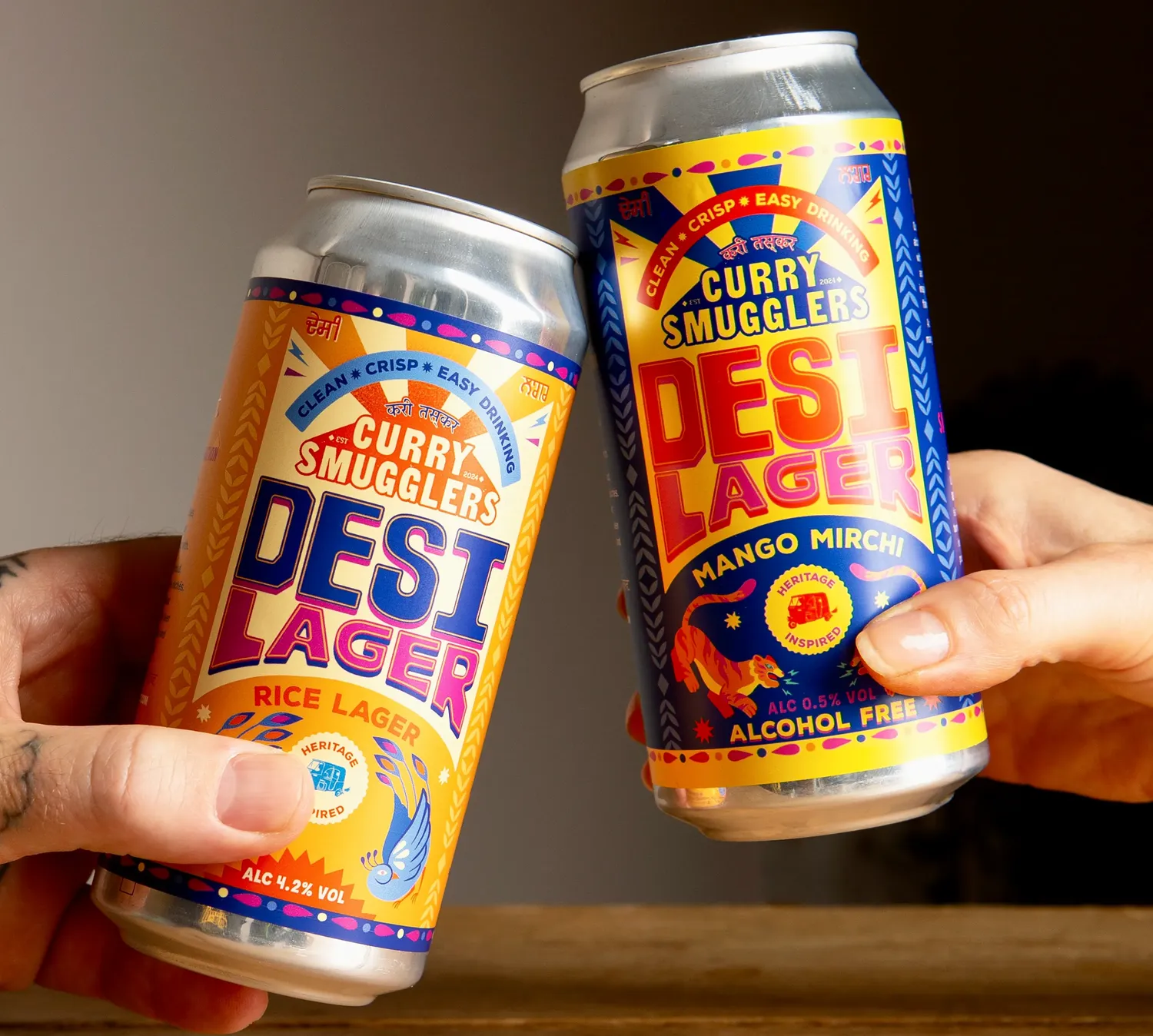 Hands holding Curry Smugglers Desi Lager cans — Rice Lager and Mango Mirchi